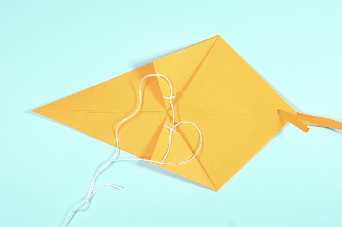 Dikiş ipliğinden bir parça kesip kanatların ucunda önceden açtığın deliklerden geçir ve düğüm at. Bu ip parçasının ortasından da iplik makarasının ucundaki ipliği düğümle. Makarada ne kadar çok ip varsa, uçurtmanı o kadar yükseğe çıkarabilirsin.